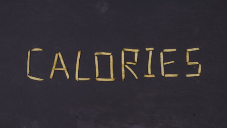 Word CALORIES laid out of long sticks of fried french fries on black background.の写真素材