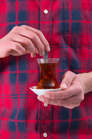 Man in red shirt is holding Turkish tea glass in his handの写真素材