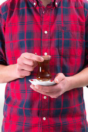 Man in red shirt is holding Turkish tea glass in his handの写真素材