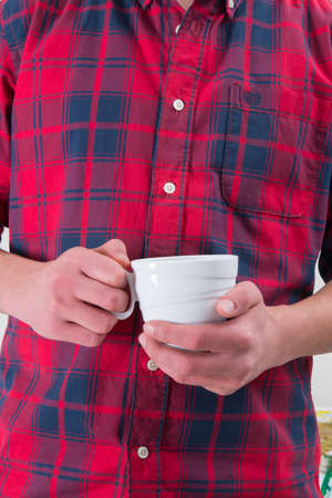Man in a red shirt is holding a white coffee mug in his hand.の写真素材