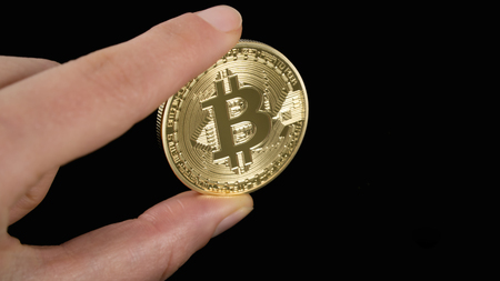 man's hand holding golden Bitcoin on black backgroundの写真素材