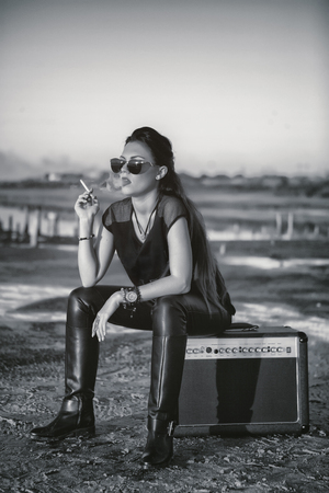 A brutal girl smokes a cigarette while sitting on the amplifier. Portrait of rock star young womanの写真素材