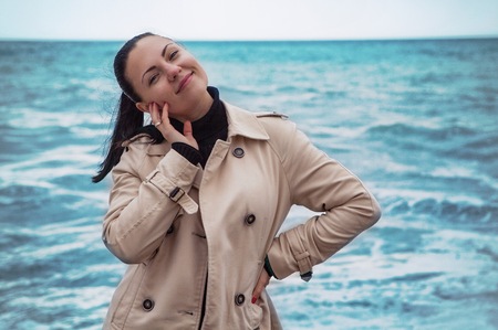 Portrait of young beautiful trendy woman standing on the sea or ocean beach and smilingの写真素材