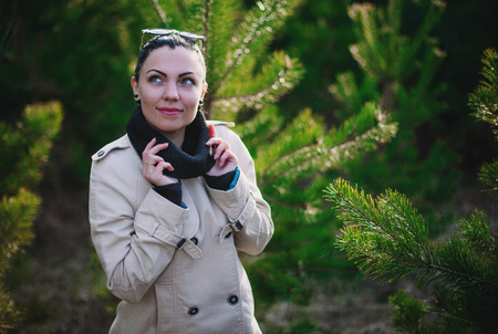 Portrait of beautiful young woman in a beige coat standing in the spruce forest.の写真素材