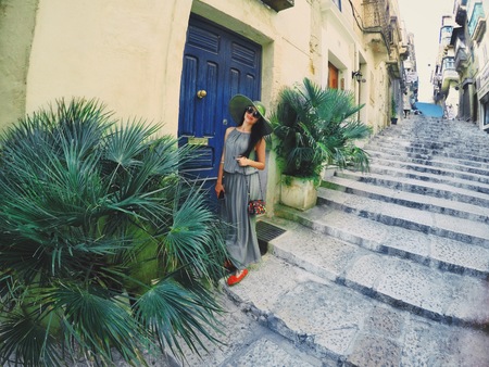 A young woman in long olive dress and hat is standing outside the old retro blue door on big stairs. Vacation and travel time.の写真素材