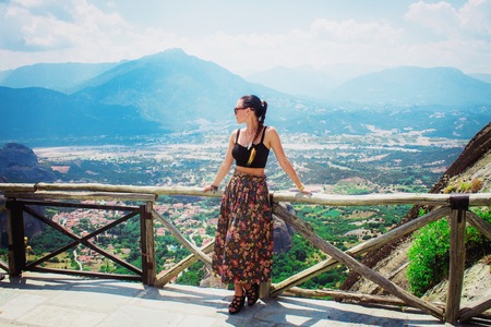 Young happy woman in long skirt stands back to the rock. Traveler enjoying the landscape with mountain, Monasteries of Meteora, Greeceの写真素材