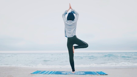 Woman standing a grateful namaste yoga pose on the beach next to the ocean or sea in cloudy weather. Zen, meditation, peace. Sun greeting - Surya Namaskar.の写真素材