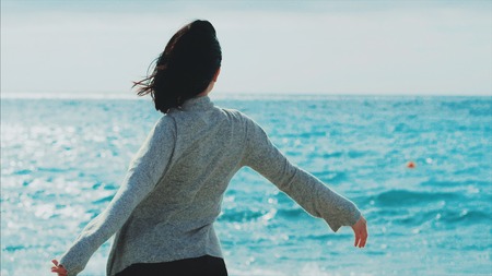 Portrait of a young brunette in warm clothing smiling woman enjoying walk on the sea beach. Real...