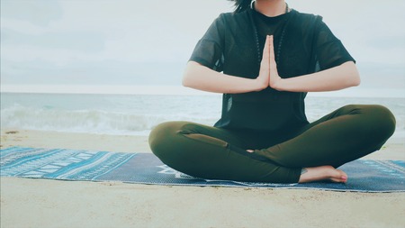 Fitness woman in sports clothing practicing yoga on the sea ocean beach close up to water. Dolly shot. Calm young woman sitting in lotus pose.の写真素材