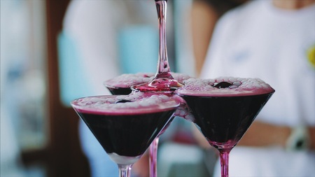Waiter pouring red wine or champagne into glasses with liquid nitrogen for party. Young man pours wine into the pyramid from the glasses.の写真素材