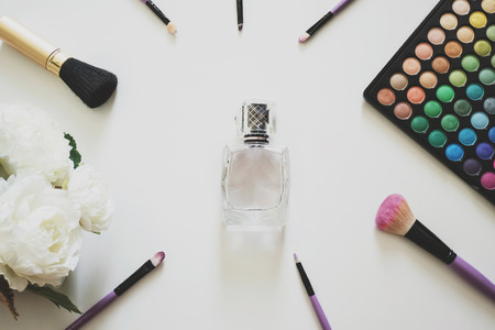 Glamour feminine cosmetic background in natural colour. Cosmetic objects frame with brushes, flowers, eye shadows, perfume bottle. Getting ready for a partyの写真素材