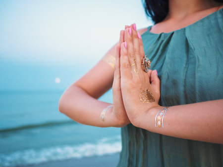 Silver and golden flash tattoo on female hands over sea or ocean background. Woman practicing yoga....