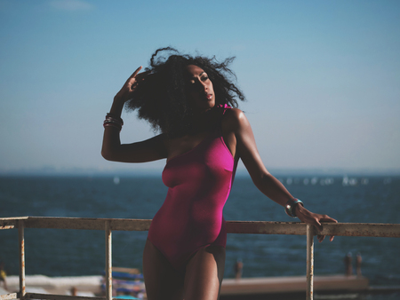 Portrait of cheerful black people, pretty happy young afro american woman smiling on sea beach. Sexy girl in pink swimsuit and jewelry enjoying nature.Lady wearing bikini.の写真素材