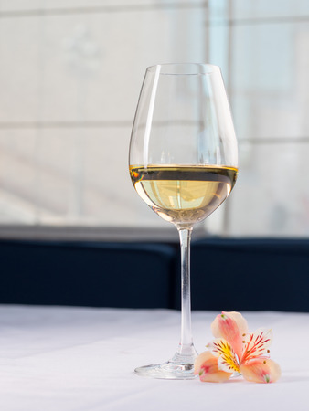 Glass of white wine on a white background and with soft shadow. Beautiful flower near on the table in restaurantの写真素材