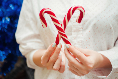 Woman holding candy canes in hands on Christmas tree background. New year concept.の写真素材