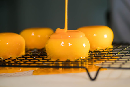 Closeup Slow Motion Shot of a Colorful Yellow Mirror Glaze Being Poured on the Frosted Desserts.
