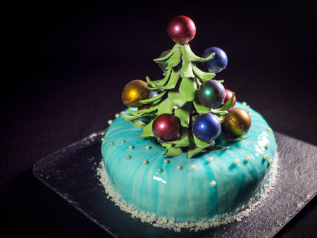 Contemporary Cake covered with blue chocolate mirror glaze and decorated with chocolate elements of Christmas tree, on dark background.の写真素材