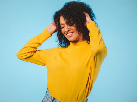 Close up portrait of laughing african american woman isolated on blue background. Mix raced girl in yellow wear posing in studio.の写真素材