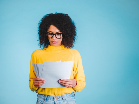 Education and business concept - international student studying in college. Or modern african american businesswoman with afro hairstyle reading documents on blue background in studio.の写真素材
