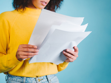 Education and business concept - international student studying in college. Or modern african american businesswoman with afro hairstyle reading documents on blue background in studio.の写真素材