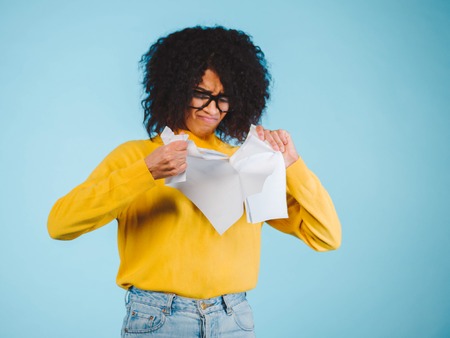 Breaking contract. Furious young african american woman with afro hairstyle tearing up paper on blue background.の写真素材
