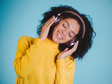 Joy and music. Colorful studio portrait of happy afro young brunette woman with earphones is dancing and singing.の写真素材