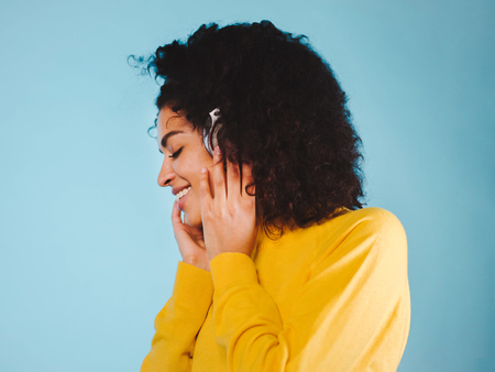 Lifestyle Concept. Portrait of beautiful african american woman joyful listening to music on mobile phone. Blue pastel studio background. Copy Space.の写真素材