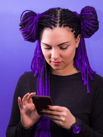 Adorable hipster caucasian female with african colorful braids hairstyle checking news feed or...
