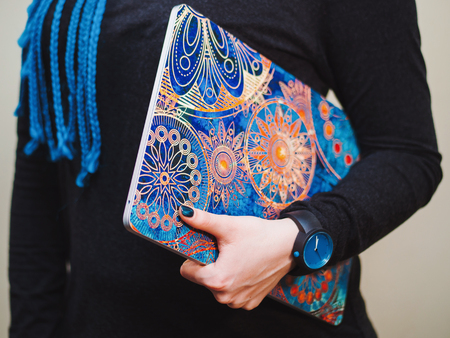 Young woman with long blue braids holding a laptop with beautiful mandala picture cover. Hands close upの写真素材