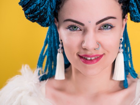Glamour portrait of sexy woman with african blue braids hairstyle, bindi, nose ring and tassel earrings isolated on yellow background. Hipster luxury girl with fur looking to camera.の写真素材