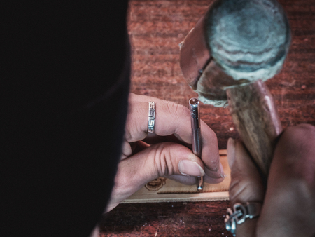 Close up of leather craftsman working with natural leather using hammer. Handbag master at work in local workshop. Handmade concept. Male shoemaker creating product with textileの写真素材