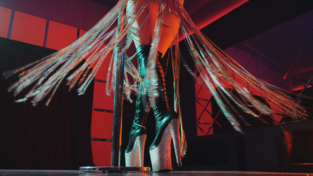 Sexy woman in high leather boots on platform heels with rhinestones.Fringe skirt with pendants made of stones.Striptease dancer moving on stage in night club with pylone.の写真素材
