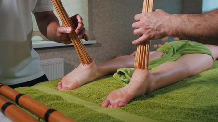 Two male masseurs working with woman. Japanese feet massage with bamboo sticks in the spa salon. People, beauty, healthy lifestyle and relaxation concept.の写真素材