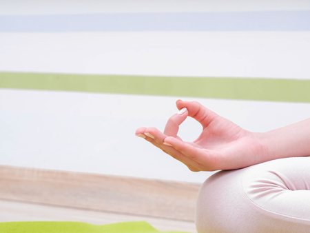 Young woman in beige jumpsuit sitting on green mat and practicing yoga at light studio class room. Meditating in lotus pose with Jnana Gian mudra. Om. Copy spaceの写真素材