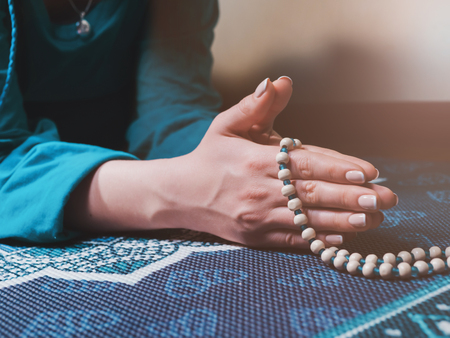 Concentrated woman praying with wooden rosary beads on yoga mat with mandala. Namaste. Close up hands. gratitude concept.の写真素材