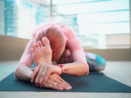 Young slim woman with pink dyed hair doing yoga practice on terrace of modern city. Girl keeping fit and healthy body relaxing on rooftop during practice poseの写真素材