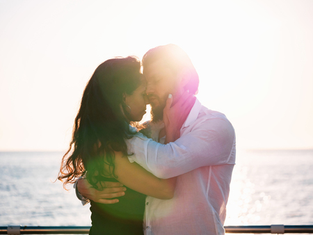Portrait of young attractive couple dancing latin bachata near sea or ocean. Sunlight background. Man gently hugs his beloved girl and looks at her with admirationの写真素材