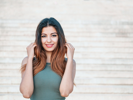 Portrait of young attractive girl looks into the camera with smile. Woman with oriental face, brown eyes and stylish ombre dyed long haistyle on architecture background. Street style.の写真素材
