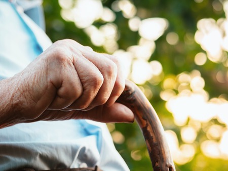 wrinkled old man' hands crossed on the stick. Close-up of a pensive grandfather sitting alone outdoors and rests on a cane.の写真素材