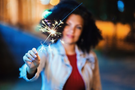Young beautiful woman with very curly afro hair dancing with bengal fire at night illuminated street. Unusual trendy girl with sparklers. Holiday concept.の写真素材