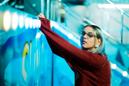 Hipster girl with blue dyed hair and sequins as freckles. Woman in red clothing and nose piercing, transparent glasses, ears tunnels, unusual hairstyle in amusement parkの写真素材