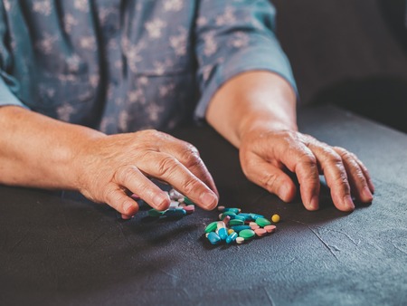 Grandmother counts multicolored tablets on black table at home. The concept of old age, medication, treatment. Close-up of hands with wrinkles.の写真素材