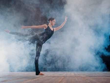 Young beautiful ballerina on smoke stage dancing modern ballet. performs smooth movements with hands...