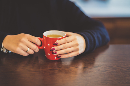 Cup of tea. Female hands holding hot drink at the kitchen.の写真素材