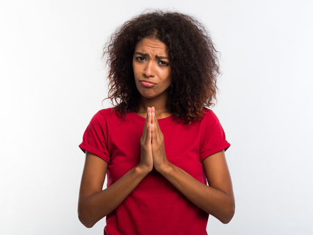 Attractive african woman in red t-shirt praying, begs over white background. Mixed race girl begging...