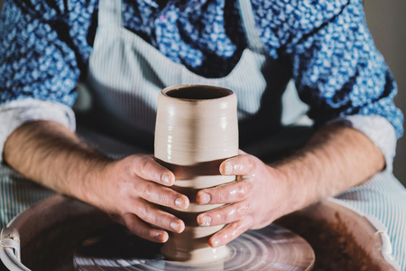 View of man making pot on pottery wheel. Potter shapes the clay product - vase - with professional tools, top view. Small business owner working in workshop.の写真素材