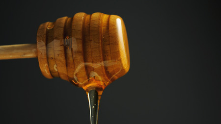 Spoon of healthy organic honey on black background. Honey dripping from wooden dipper close-up.の写真素材