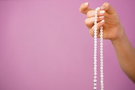 Woman, lit hand close up, counts Malas, strands of gemstones beads used for keeping count during mantra meditations on pink backgroundの写真素材