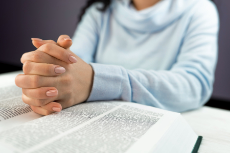 Unrecognizable woman reading big book - Holy Bible and praying. Christian studying scripture....