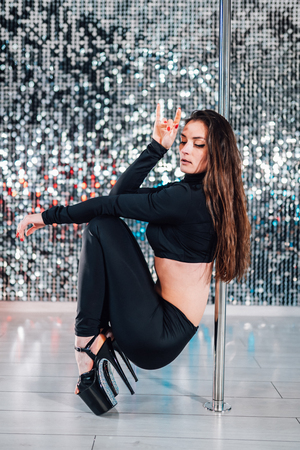 Alluring woman with long hair posing with pylon on shining wall background. Pole-dance, sexy, temptation concept.の写真素材
